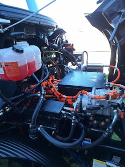 Under the hood are the electrically driven A/C compressor (lower right) and, on the left side behind a lithium-ion battery pack, the power steering pump. A common reservoir for windshield wiper fluid is at left. Under the hood are the electrically driven A/C compressor (lower right) and, on the left side behind a lithium-ion battery pack, the power steering pump. A common reservoir for windshield wiper fluid is at left.