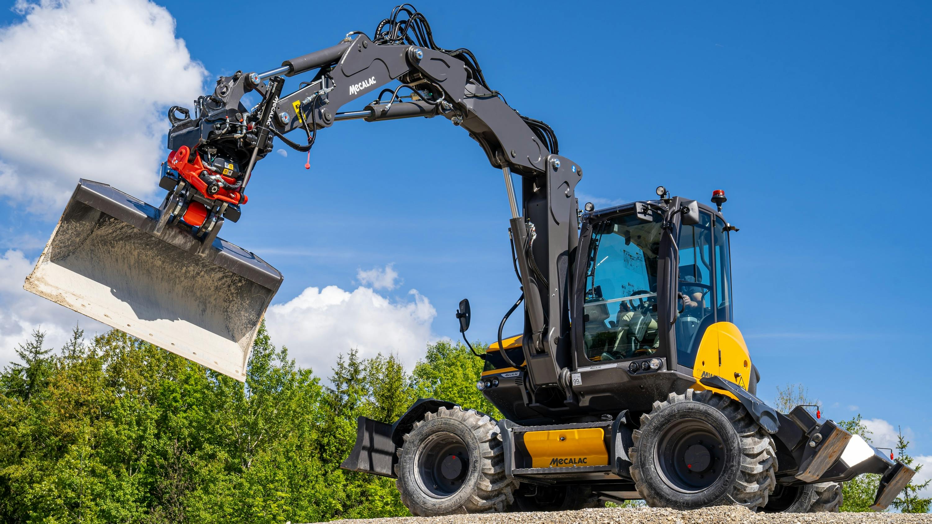 Mecalac tiltrotators operating on site with a bucket attachment.
