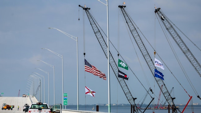 A green flag with the company logo for Archer Western Construction hangs from a crane near another flag for the Florida Department of Transportation, next to the new lanes of the new Howard Frankland Bridge on March 24, 2025. A Tampa Bay Times investigation about Archer Western has prompted Florida politicians to call for state officials to hold the company accountable.
