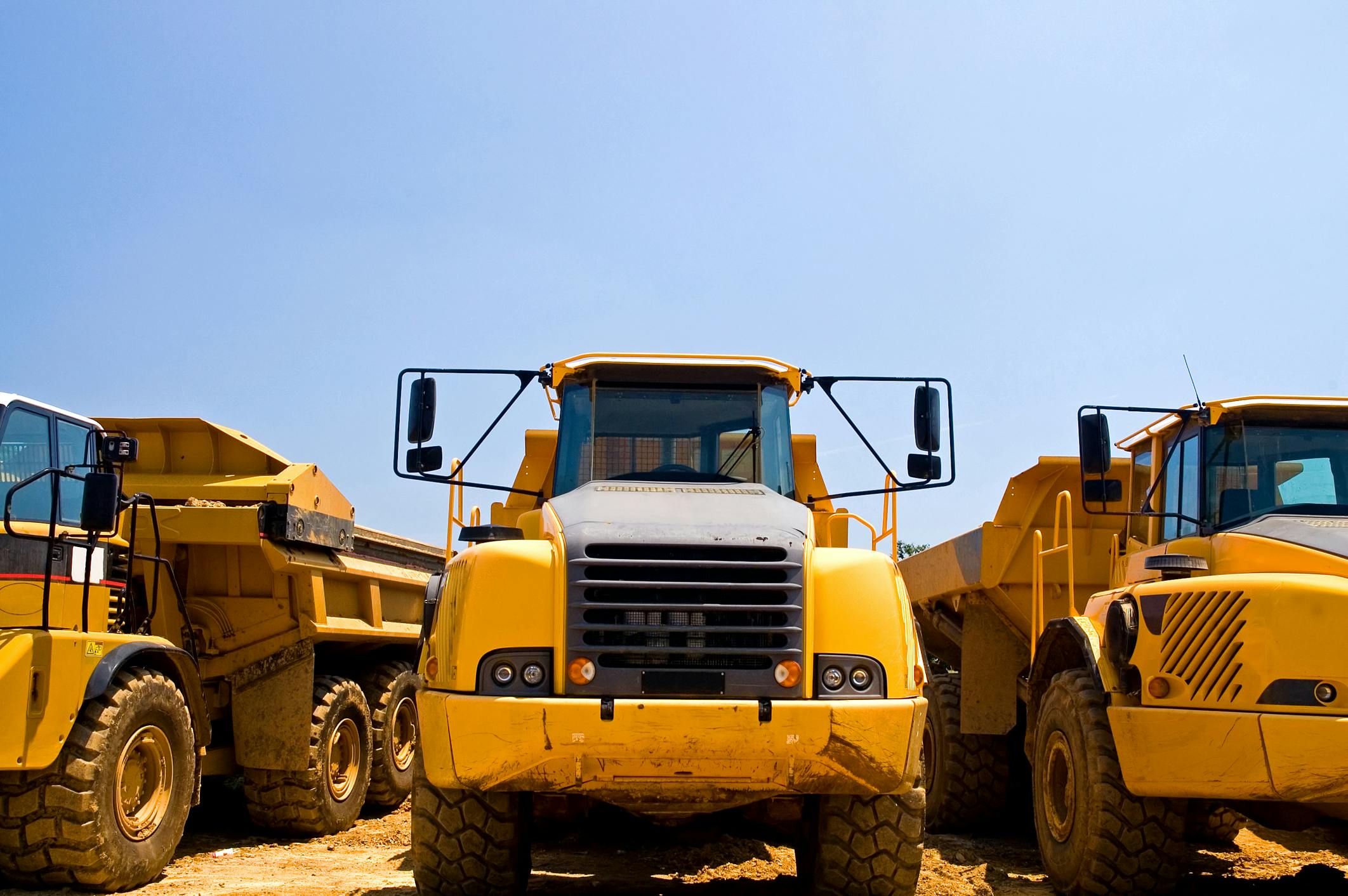 Heavy duty construction trucks. A view of the front of yellow, heavy duty earthmoving trucks on a construction site.