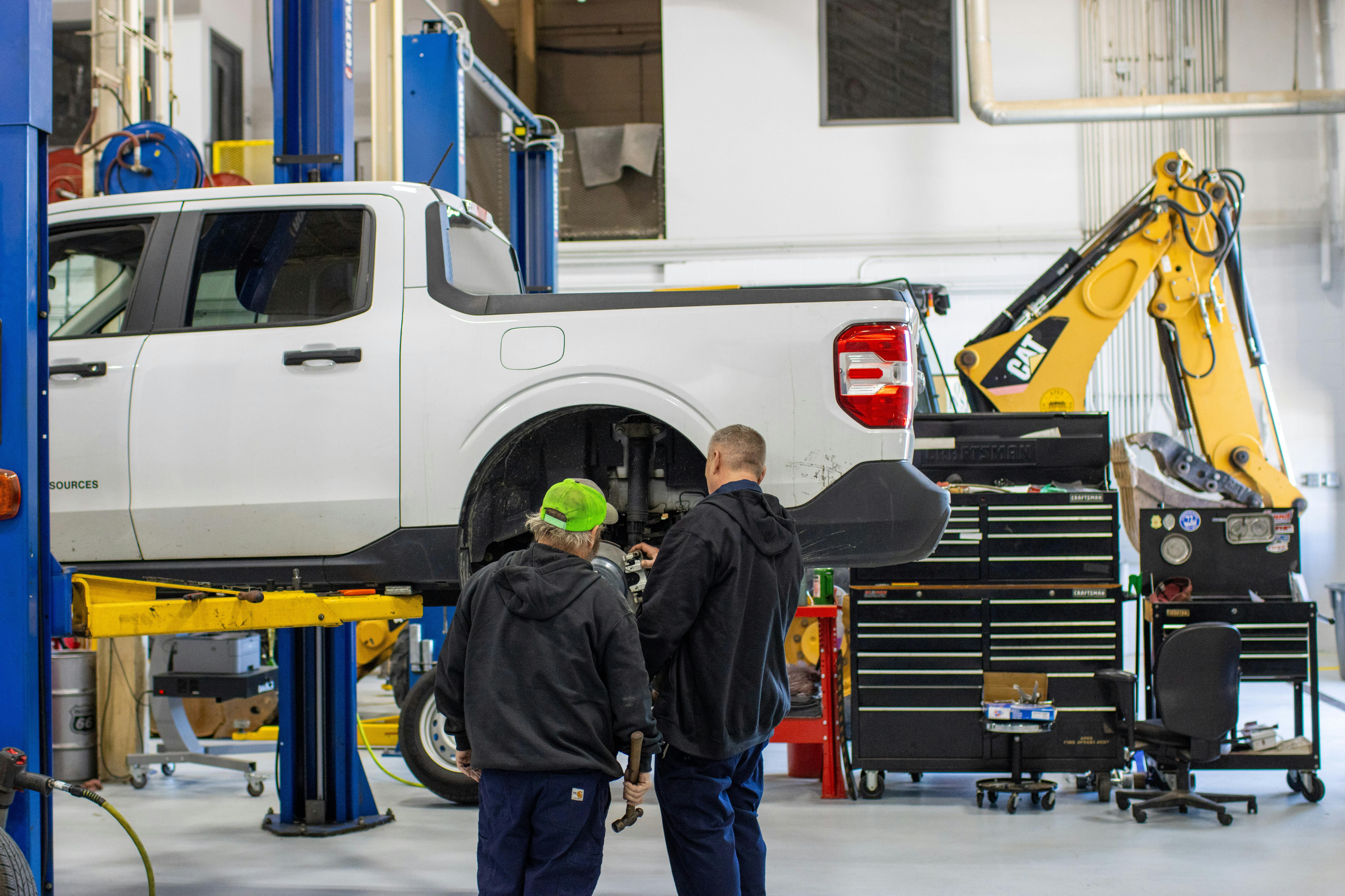 Fleetio&rsquo;s 2026 Fleet Benchmark Report two mechanics inspect a truck, a Cat backhoe sits in the background