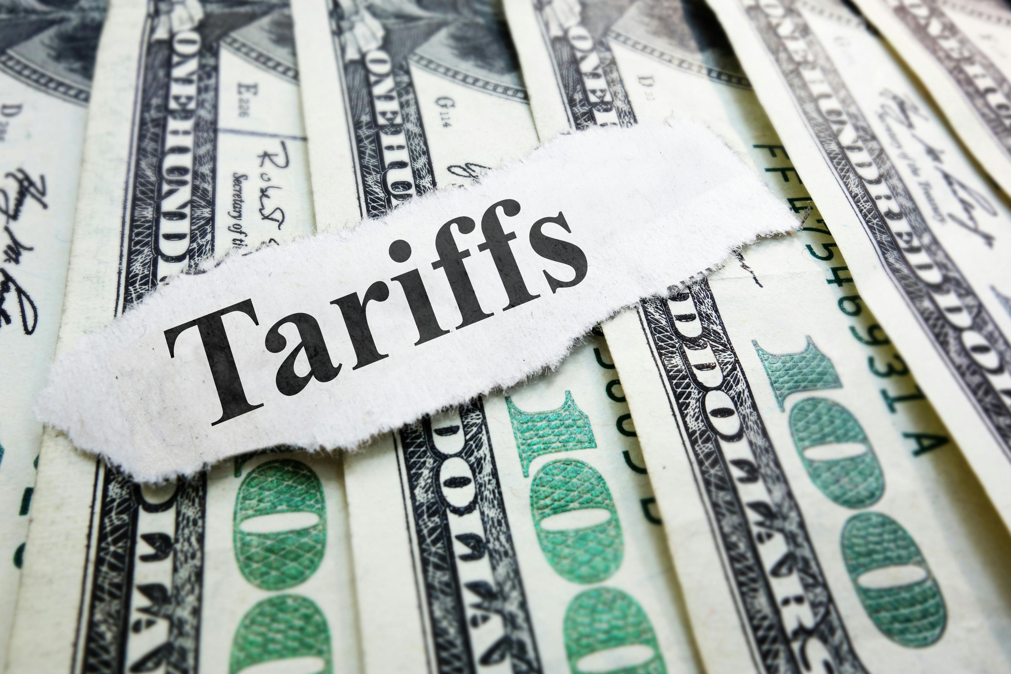 Money laying on a surface with a piece of paper that says Tariffs.