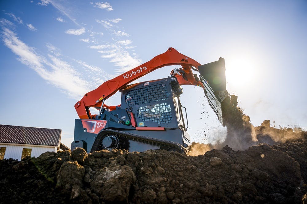 Kubota SVL110 compact track loader dumping dirt in the sun.