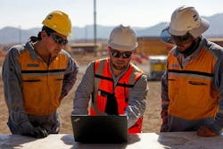 Contractors with Cat helmets look at a laptop. Contractors with Cat helmets look at a laptop.