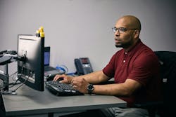 Man types on a computer, looks at monitor with toy excavator. Man types on a computer, looks at monitor with toy excavator.