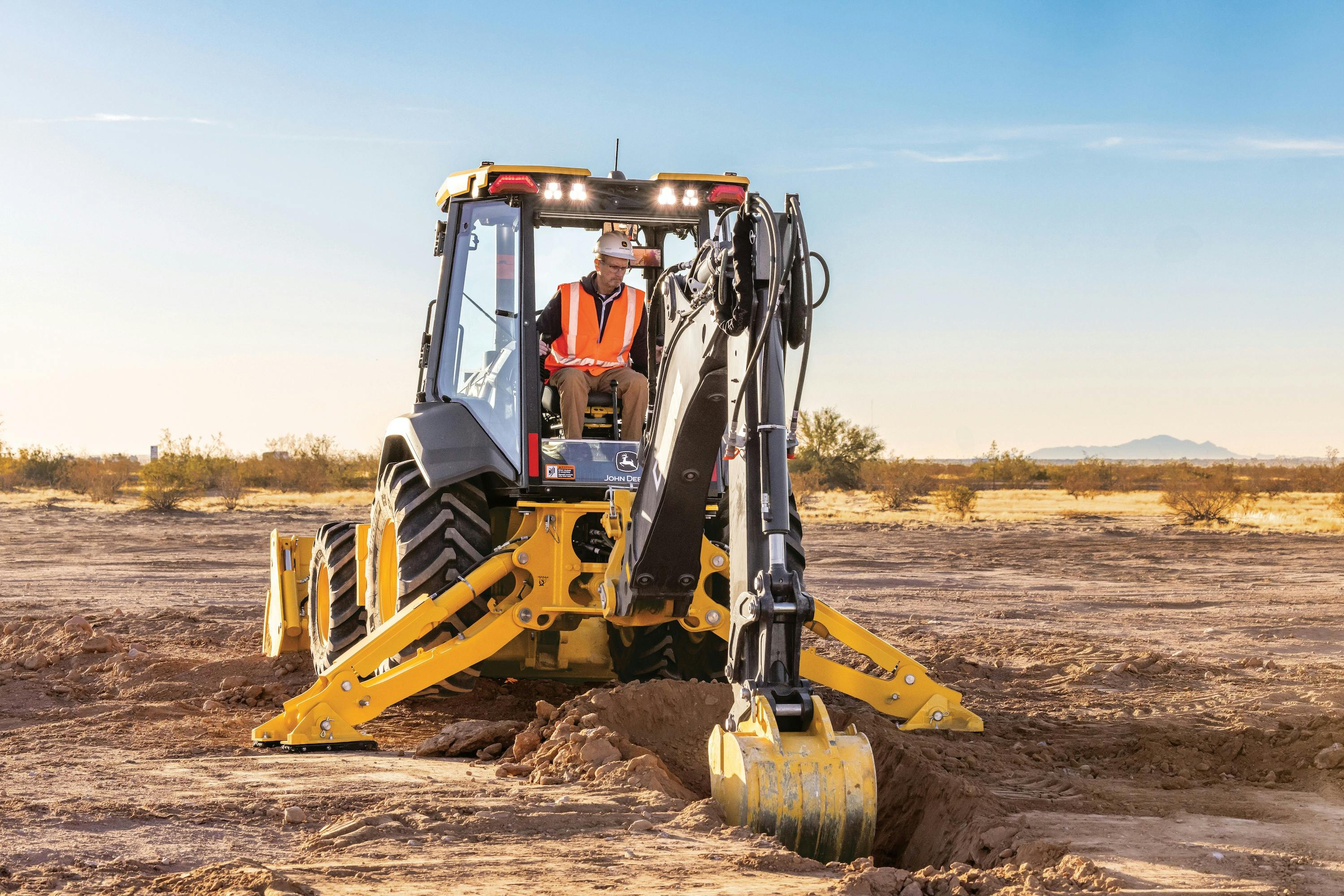 John Deere backhoe loader digging in the dirt on the backhoe side.
