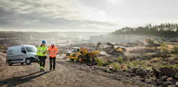 Volvo Construction Equipment machines work a jobsite while two men talk Volvo Construction Equipment machines work a jobsite while two men talk