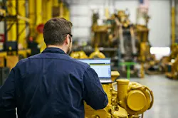 Caterpillar mechanic on a computer, sitting on an engine Caterpillar mechanic on a computer, sitting on an engine