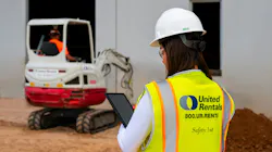 United Rentals agent on tablet with a mini excavator in the background. United Rentals agent on tablet with a mini excavator in the background.