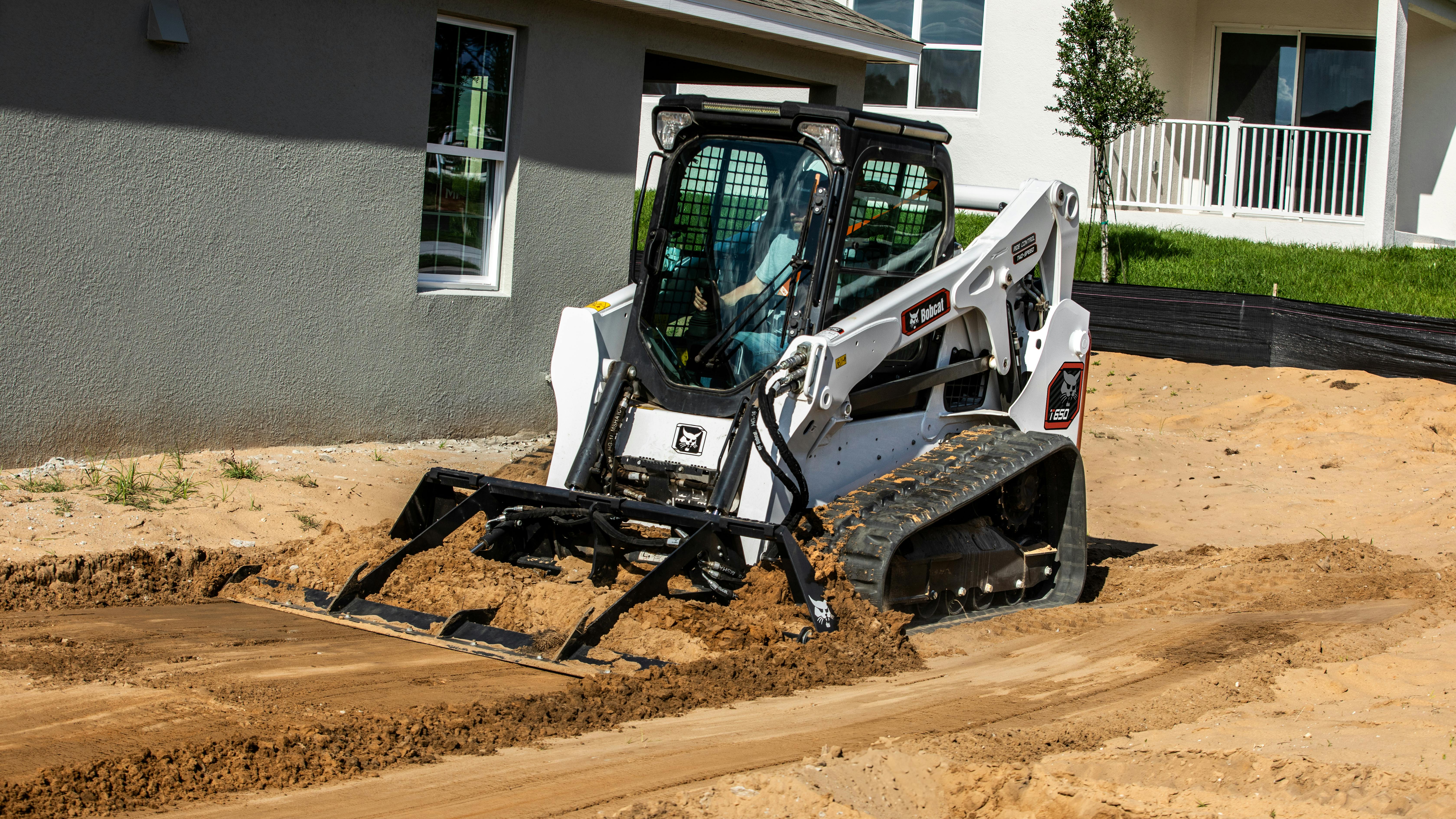Bobcat T650 using a land plane to grade dirt near houses.