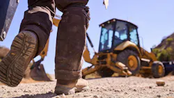 Man walking toward a Caterpillar backhoe in the dirt. Man walking toward a Caterpillar backhoe in the dirt.