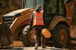 Mechanic walking up to a Caterpillar backhoe loader. Mechanic walking up to a Caterpillar backhoe loader.