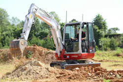 Takeuchi TB240 compact excavator digging dirt in a field. Takeuchi TB240 compact excavator digging dirt in a field.