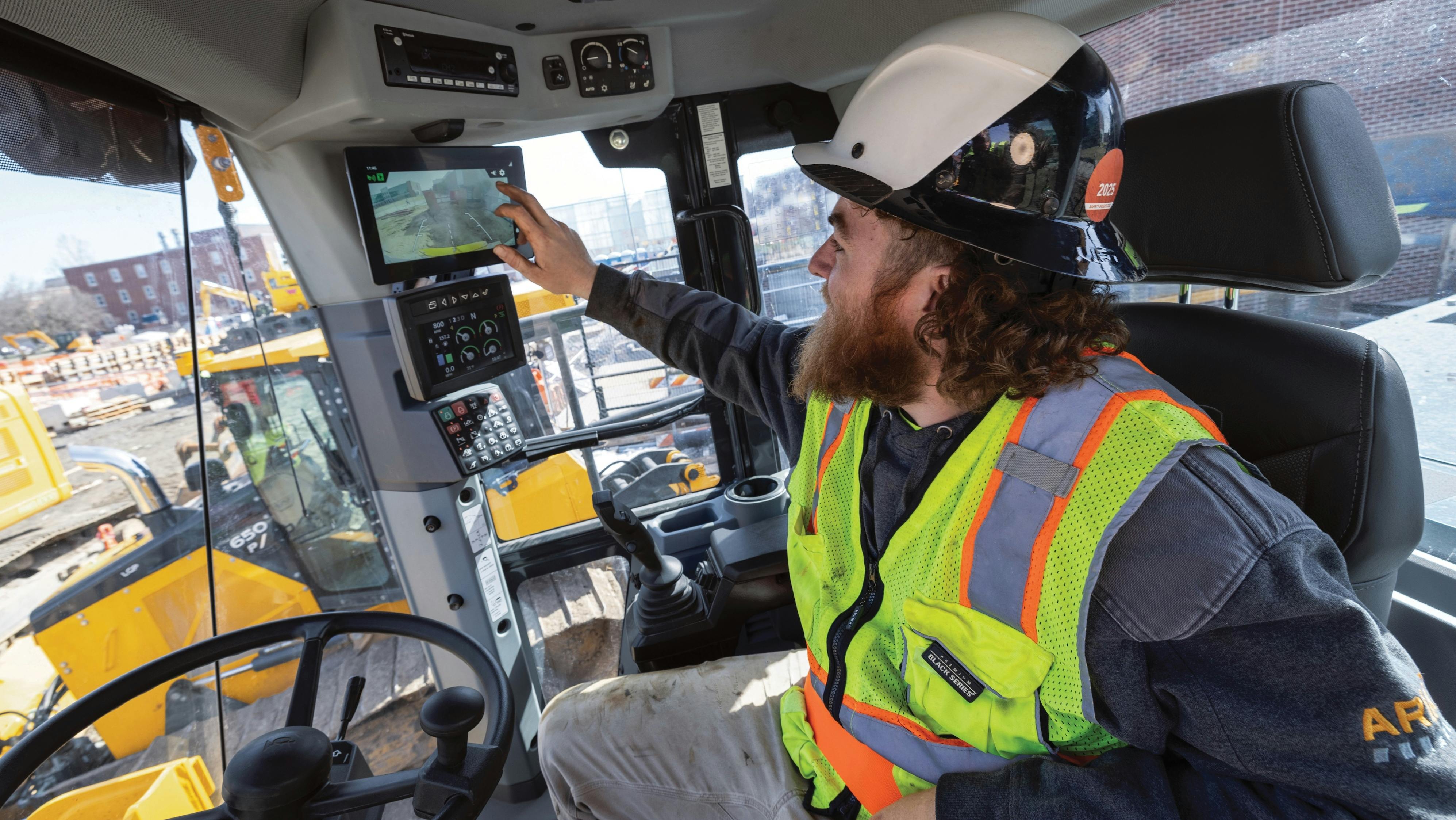 John Deere wheel loader equipped with AI camera system. Operator examines the camera monitor.