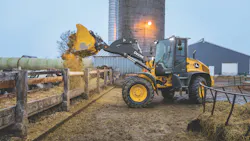 John Deere 344 P-Tier wheel loader dumping hay over a fence at a farm.