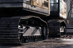 Close view of excavator steel tracks on a muddy jobsite, illustrating construction equipment wear, industrial workflow and fleet support