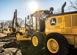 John Deere motor grader with an excavator in the background.