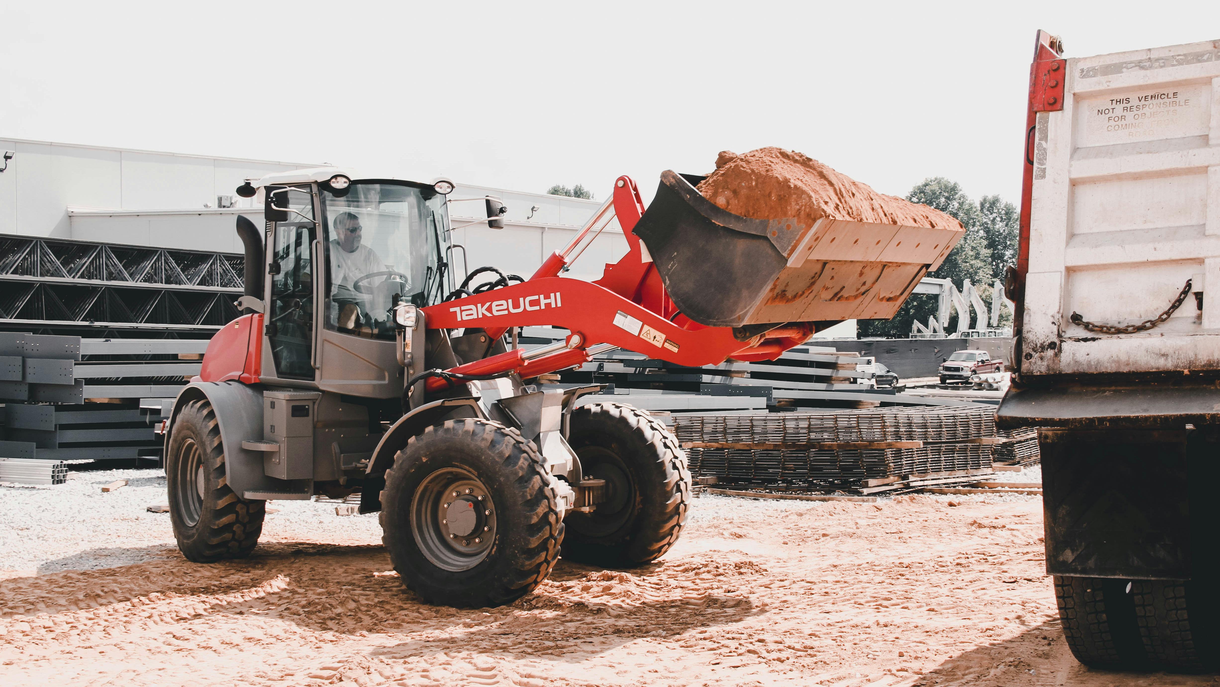 Takeuchi compact wheel loader carrying fresh dirt to a dump truck.