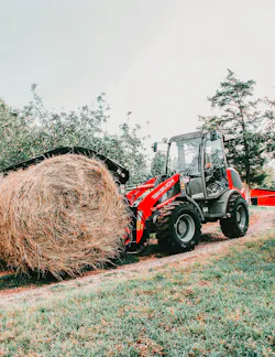 Takeuchi compact wheel loader carrying a bale of hay.