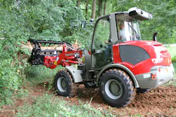 Takeuchi TW60 grabbing logs in a forest.