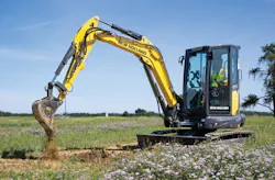 New Holland Construction mini excavator digging dirt in a pasture.