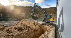Volvo Construction Equipment excavator digging a utility trench next to a building.