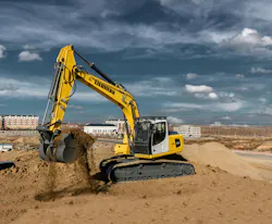 A Liebherr excavator digs dirt with the sky and city in the background.