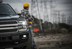 Construction worker looking off into the distance, leaning on a truck.