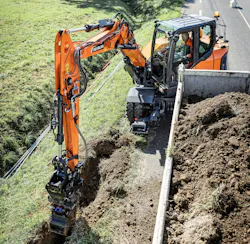 Develon DX100W-7 wheeled excavator digging a trench by the street.