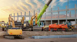 Many different multiclored colorful heavy industrial machinery equipment at construction site parking area against warehouse building city infrastructure development. Commercial vehicles rental sale.