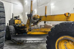 An old grader is getting serviced in an industrial garage.