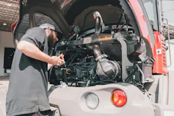 A mechanic works on a Takeuchi compact wheel loader, checking oil.