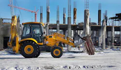 A backhoe driving through a wintery construction site.