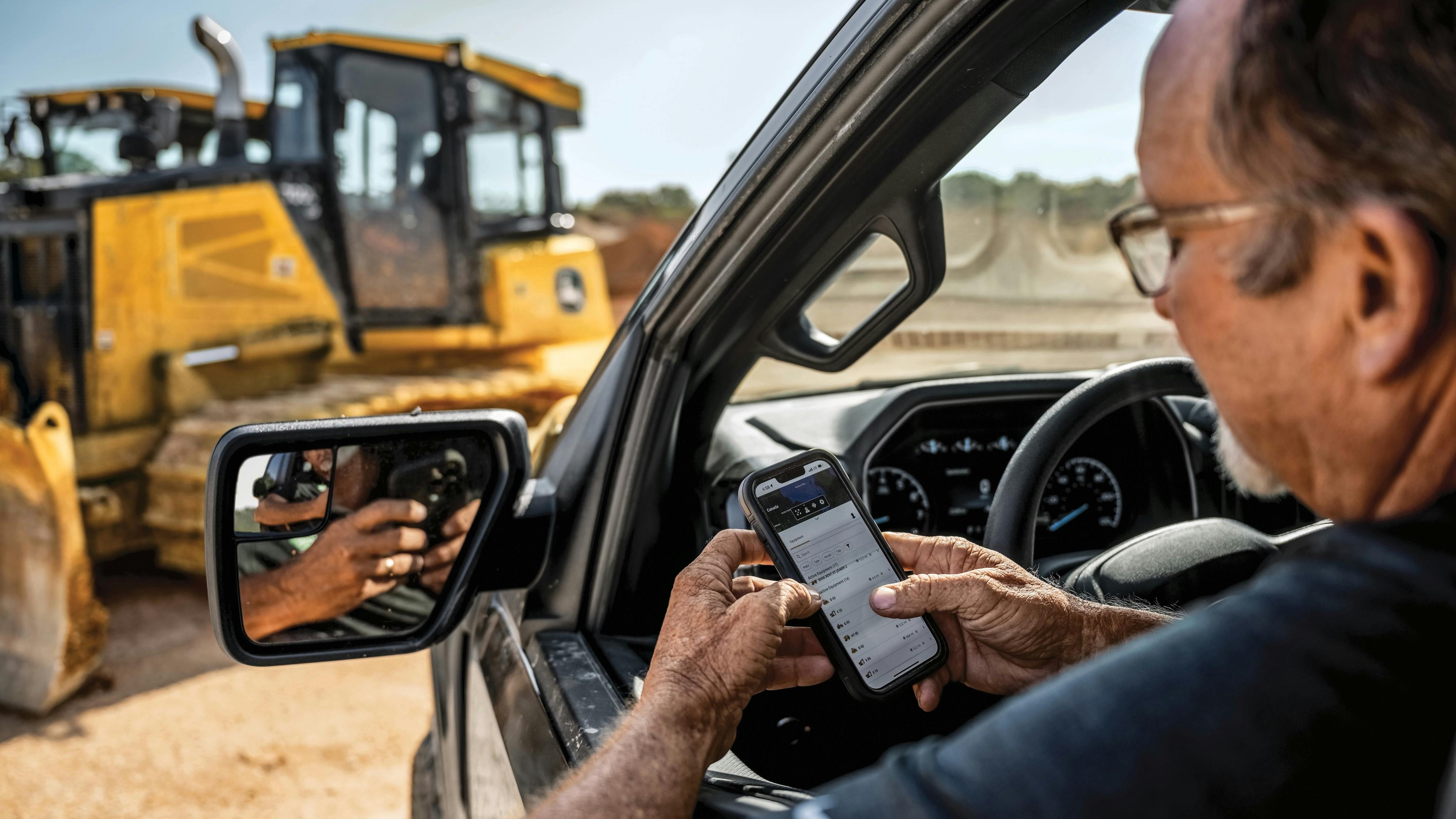John Deere Operations Center. Man checks his phone while looking at a John Deere dozer.
