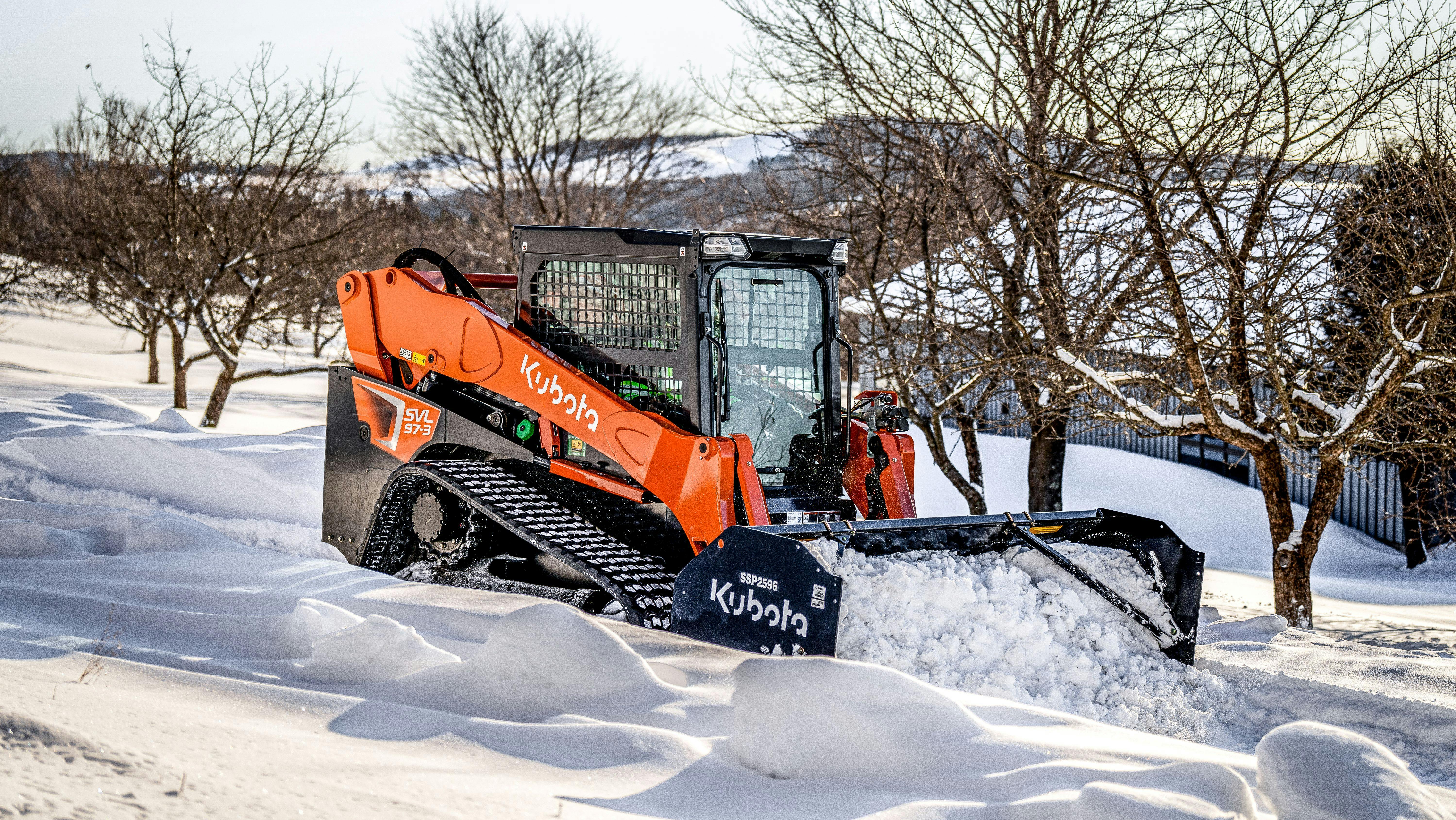 Kubota SVL97-3 compact track loader with a snow pusher attachment, cleaning up snow.