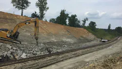 An excavator breaks rock near a railroad