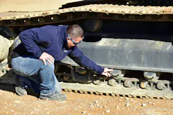 A mechanic inspects a Develon excavator's rollers for wear and tear.