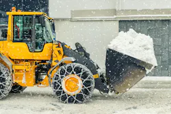A wheel loader with chains on its tires carries snow in its bucket.