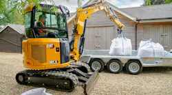 Caterpillar 302.6 mini excavator lifting bags onto a trailer.