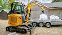 Caterpillar 302.6 mini excavator lifting bags onto a trailer.