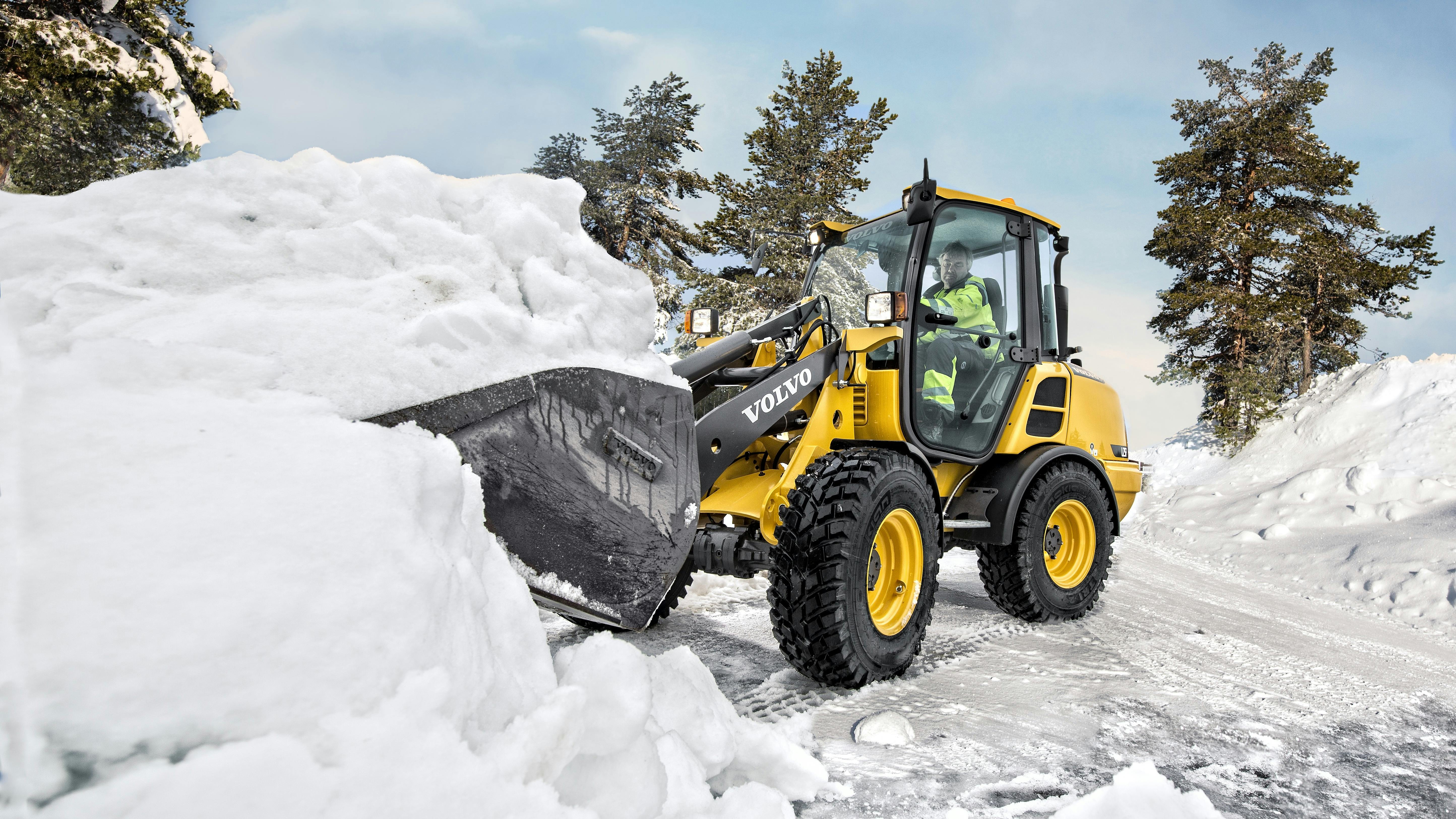 A Volvo compact wheel loader digging into a pile of snow.