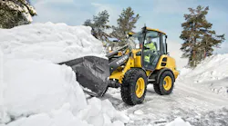 A Volvo compact wheel loader digging into a pile of snow.