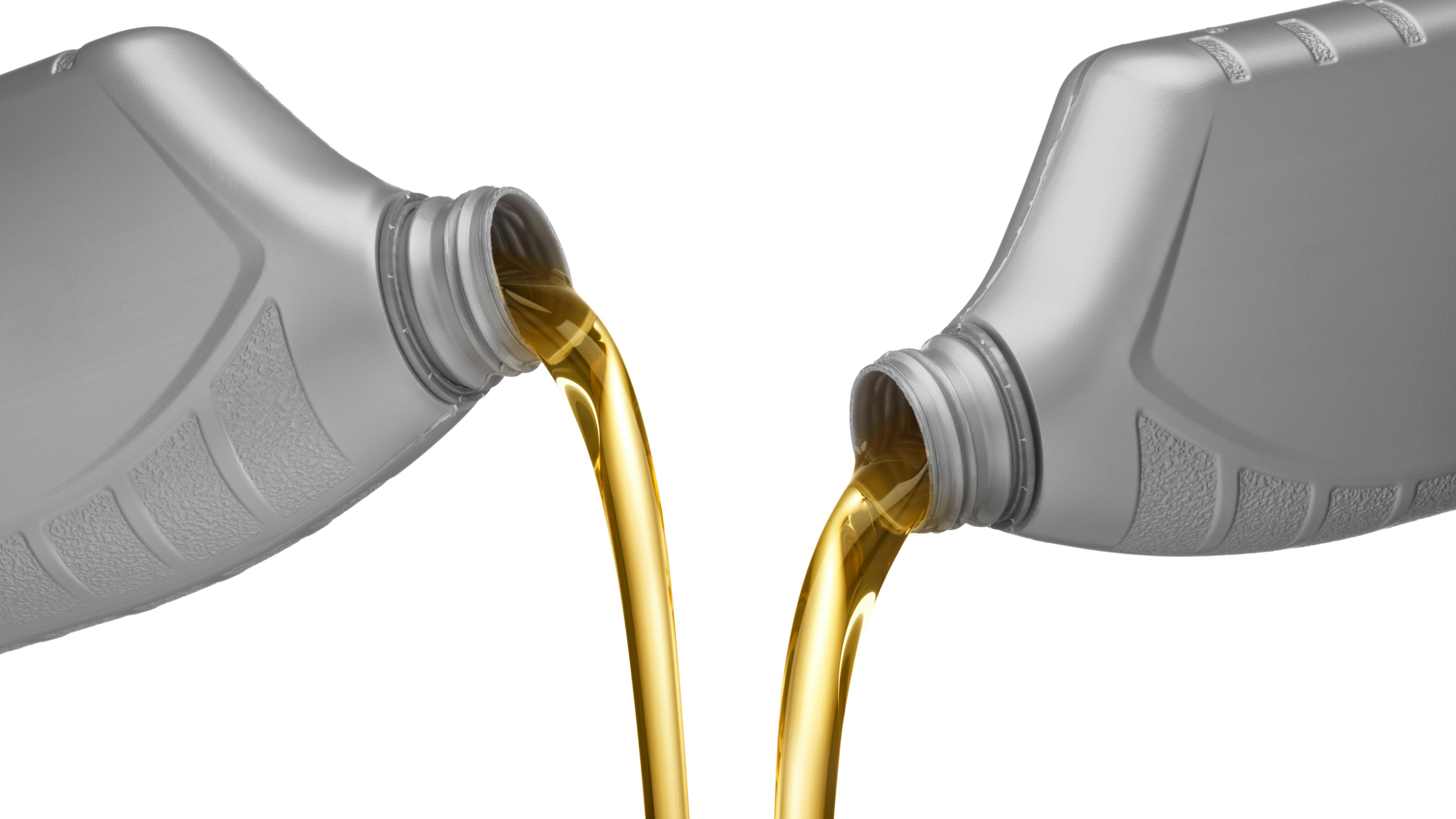 Two oil bottles are being poured on a white background.
