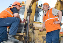 Two mechanics talk around a backhoe loader.