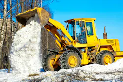 A wheel loader unloading snow on the side of the road.