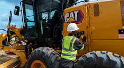 A mechanic looks to inspect a Caterpillar 140 motor grader.