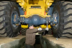 A mechanic works on the axle of a motor grader.