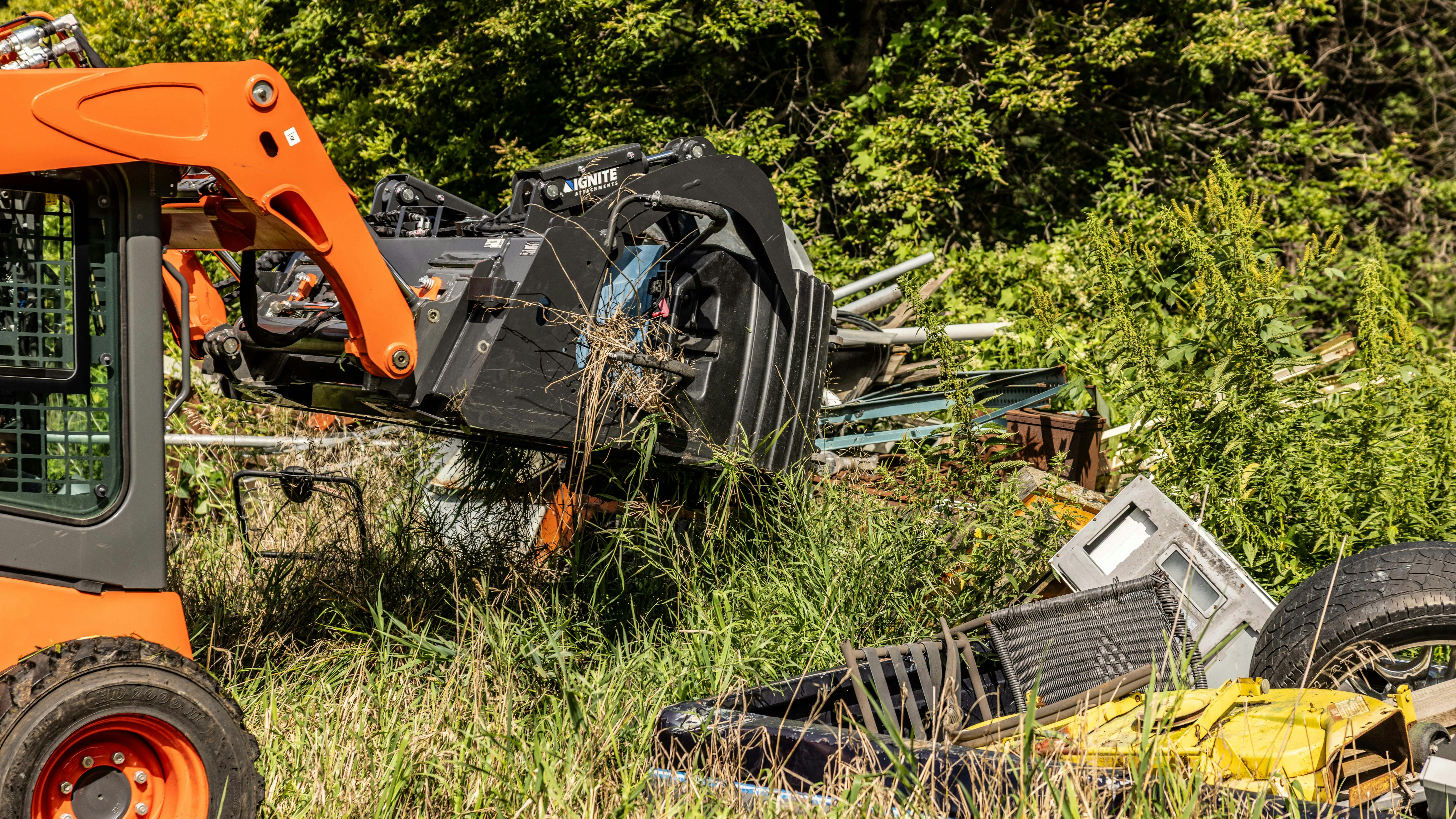 A skid steer grabs garbage with an Ignite grapple bucket.