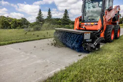 A Kubota skid steers uses an Ignite broom attachment to clean up grass clippings.