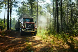 A Volvo Trucks VNX 300 carrying logs, rolling down a wooded road.